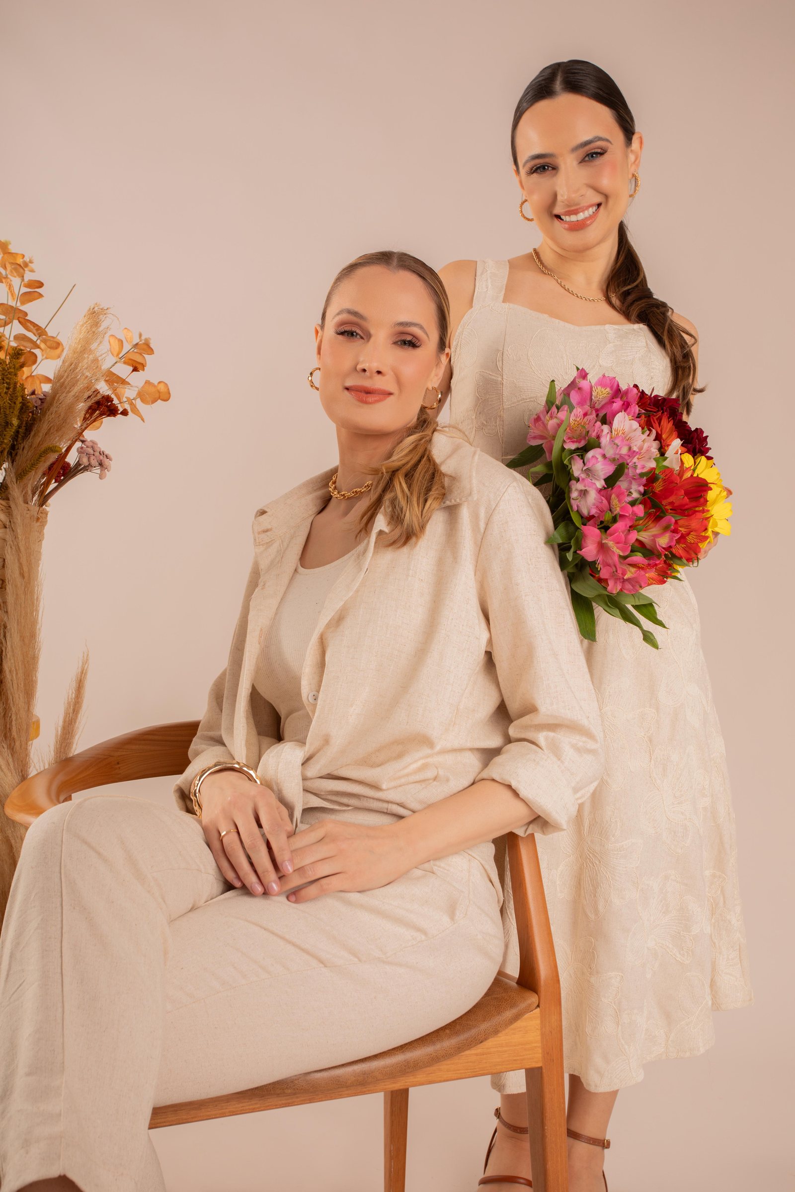 Duas modelos com looks bege, uma segurando um buquê